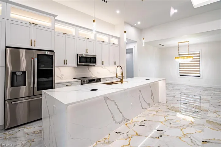 Gourmet kitchen with a waterfall island, stainless steel appliances, white cabinetry, and gold-tone hardware