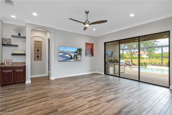 Large family room with floating shelves, crown molding, designer ceiling fan, and fabulous view of the outdoor living space and lake beyond.