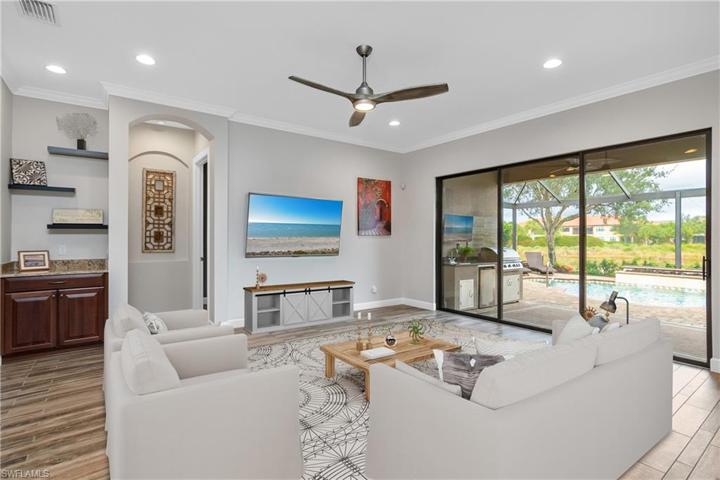 Large family room with floating shelves, crown molding, designer ceiling fan, and fabulous view of the outdoor living space and lake beyond. (photo digitally staged)