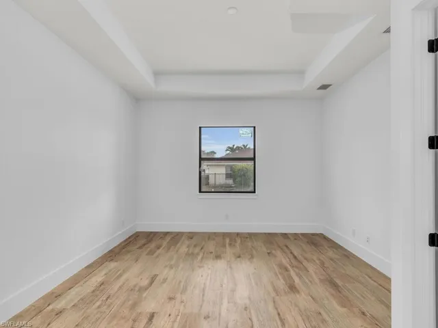 Empty room with baseboards, visible vents, wood finished floors, and a raised ceiling