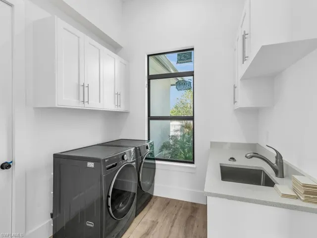 Washroom featuring baseboards, a sink, light wood-type flooring, cabinet space, and washer and clothes dryer