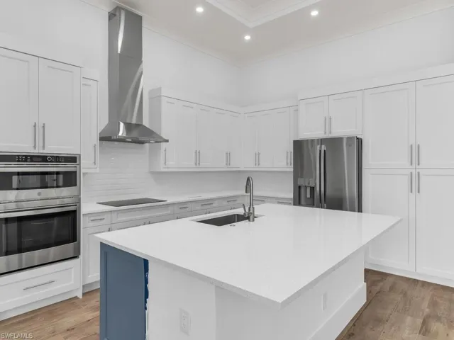 Kitchen featuring wall chimney range hood, light countertops, a sink, and appliances with stainless steel finishes