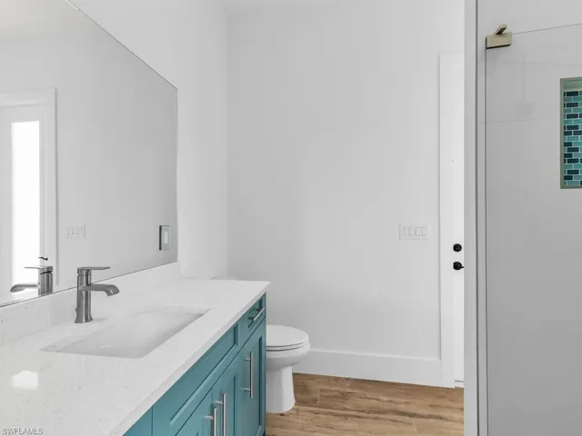 Full bathroom with walk in shower, baseboards, wood finished floors, toilet, and vanity