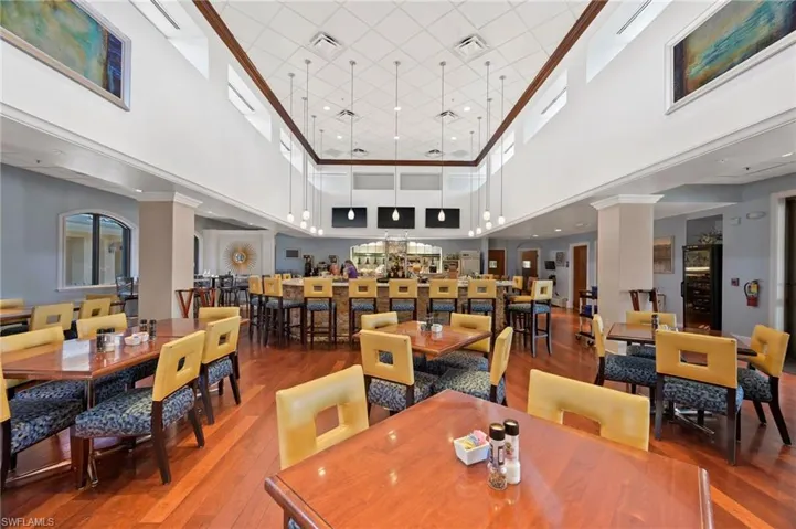 Spacious dining area featuring wood-finish flooring, a full-service bar with stone-clad front, high ceilings with clerestory windows, and modern pendant lighting