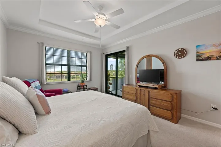 Recessed tray ceiling with crown molding, ceiling fan with integrated lighting, wall-to-wall carpeting, and sliding glass doors leading to a private balcony