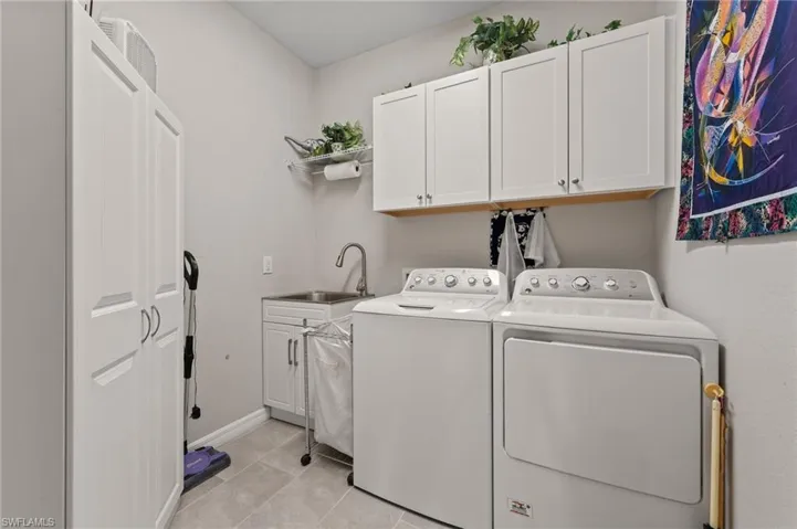 White shaker-style cabinetry, stainless steel utility sink, gooseneck faucet, and light tile flooring