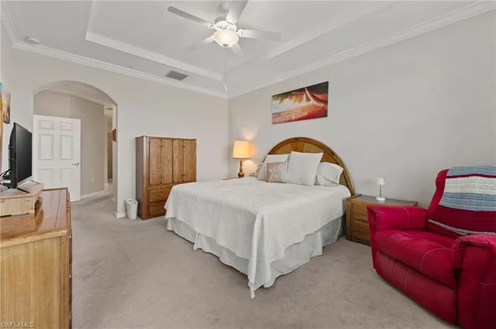 Tray ceiling with crown molding, ceiling fan with integrated lighting, arched doorway, and neutral carpet flooring