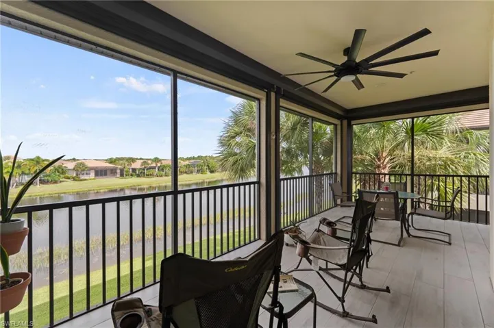 Screened outdoor living area with a ceiling fan, white tile flooring, and a black metal railing overlooking a body of water