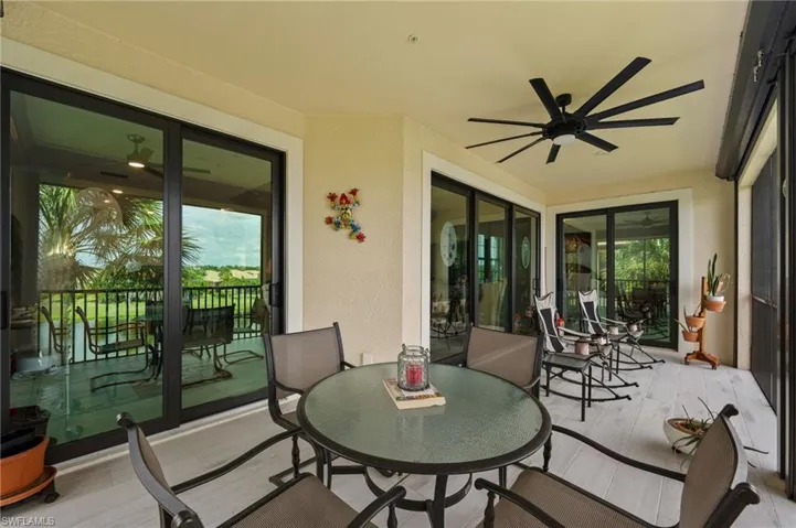 Expansive covered patio featuring light-toned flooring, multiple sets of sliding glass doors, and a large ceiling fan