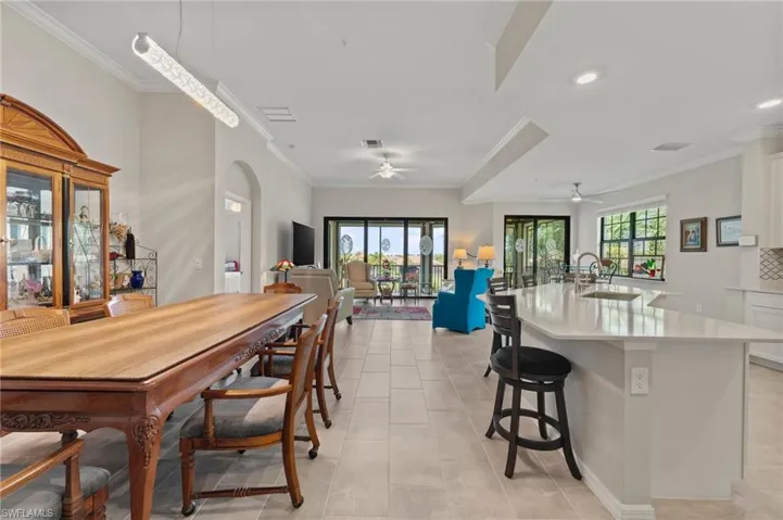 Open-concept layout featuring neutral tile flooring, crown molding, a kitchen island with seating, and sliding glass doors