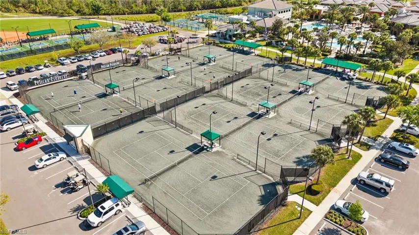 Multiple tennis courts with perimeter fencing, shaded viewing areas, and adjacent parking