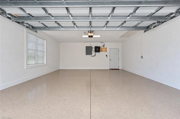 Spacious garage featuring a durable epoxy floor coating, white block walls, a side-mounted window with horizontal blinds, and an interior access door