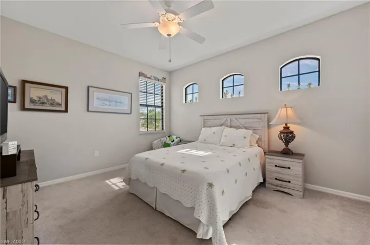 Arched windows, single rectangular window with blinds, ceiling fan with integrated lighting, and textured wall-to-wall carpeting