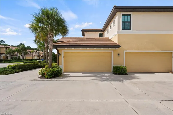 Stucco exterior with two garage doors, concrete driveway, and mature palm tree landscaping