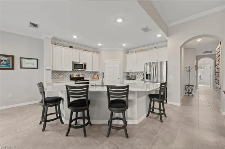 Kitchen featuring white cabinetry, stainless steel appliances, a geometric tile backsplash, and an island with a light-toned countertop