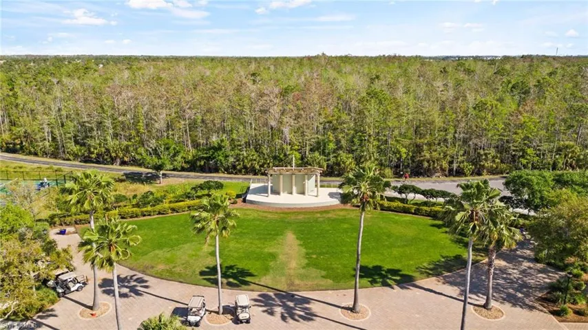 Manicured green space with mature palm trees, a pavestone entry, and a contemporary open-air structure, all bordered by extensive natural landscaping
