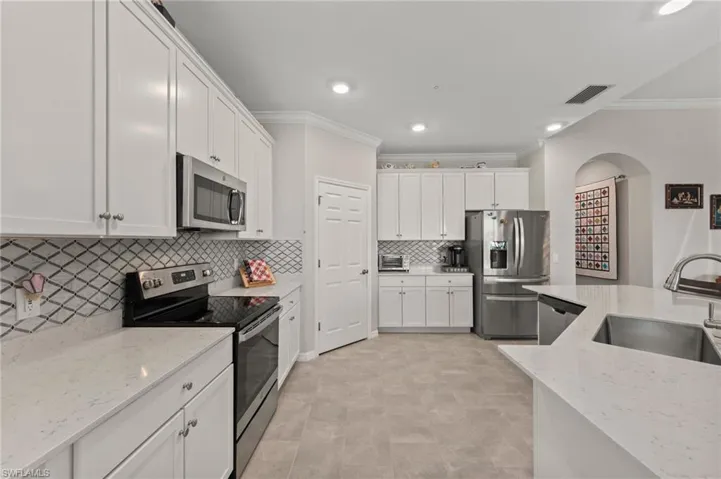 Bright kitchen featuring white cabinetry, light-toned countertops, stainless steel appliances, a decorative tile backsplash, and recessed lighting