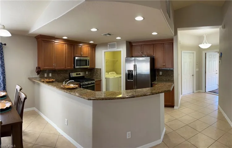 Kitchen featuring backsplash, appliances with stainless steel finishes, washer and clothes dryer, and dark stone counters
