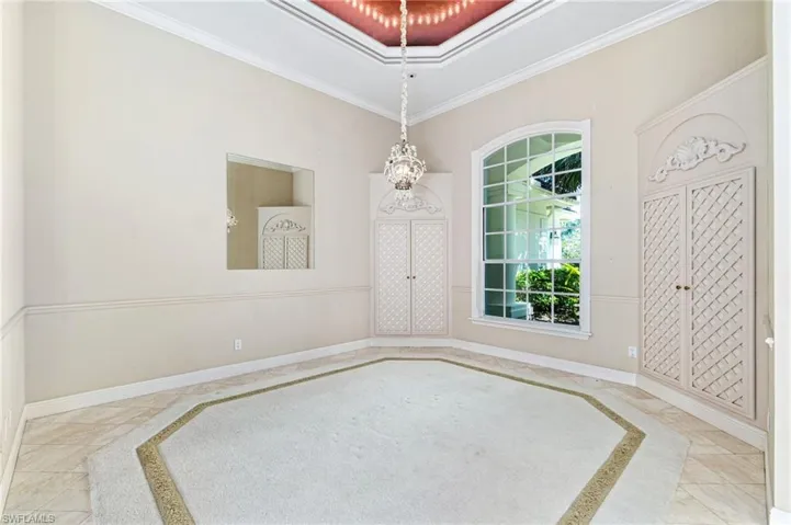Empty room featuring a raised ceiling, ornamental molding, and tile floors