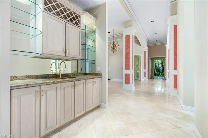 Bar with dark stone counters, light tile flooring, decorative columns, and crown molding