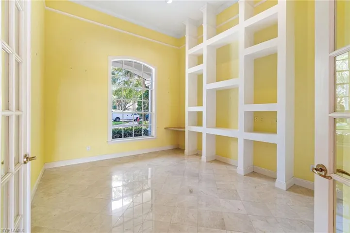 Tiled empty room featuring plenty of natural light, built in shelves, and crown molding