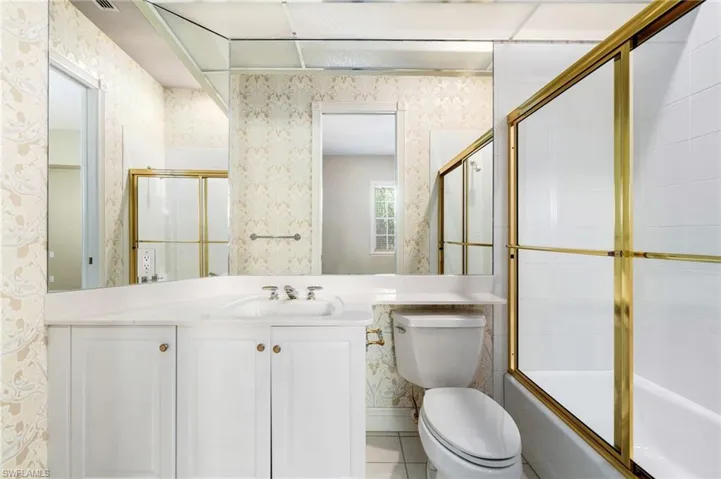 Full bathroom with enclosed tub / shower combo, tile flooring, vanity, and toilet