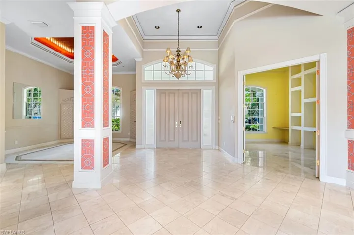 Foyer with a notable chandelier, ornamental molding, ornate columns, and light tile floors