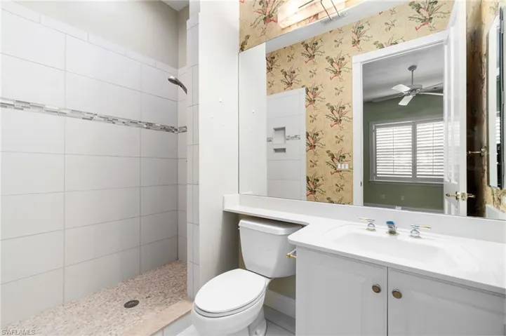 Bathroom featuring a tile shower, ceiling fan, toilet, and vanity