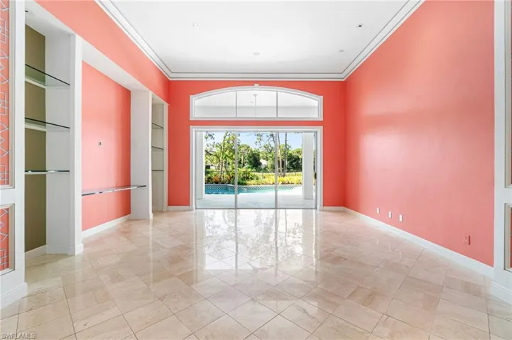 Empty room with crown molding, built in shelves, and light tile floors