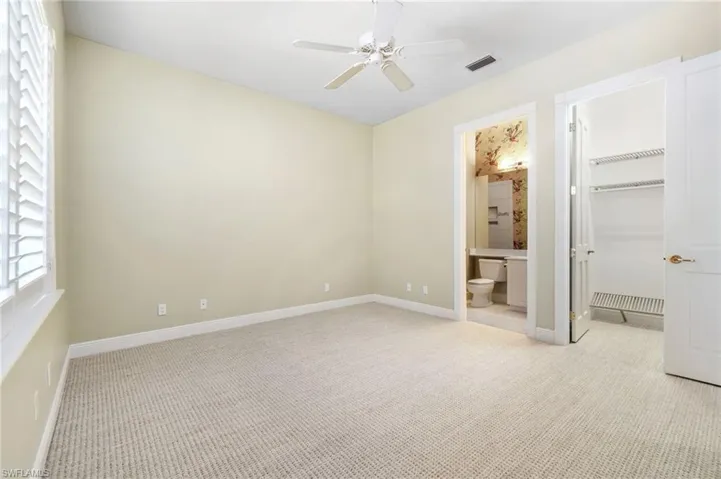 Unfurnished bedroom featuring a closet, ensuite bathroom, ceiling fan, a walk in closet, and light carpet