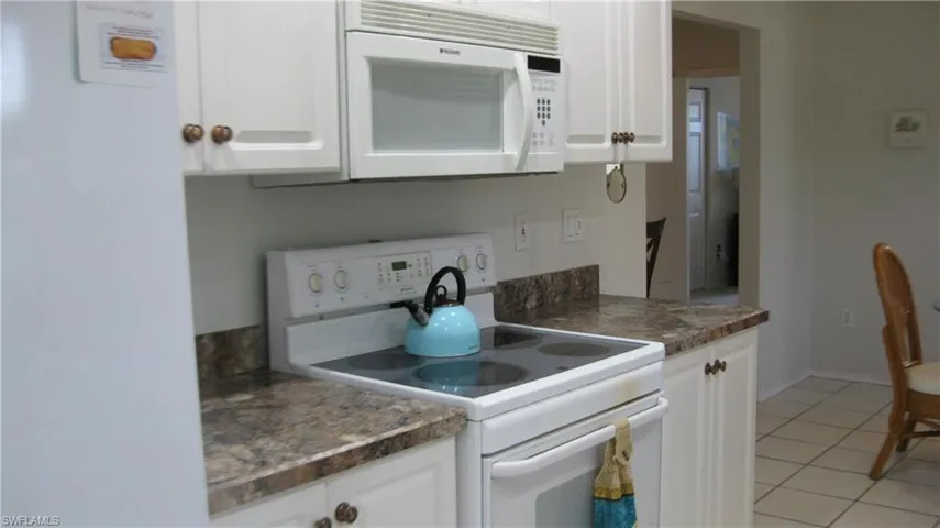 Kitchen featuring white appliances, dark countertops, white cabinetry, and light tile patterned flooring