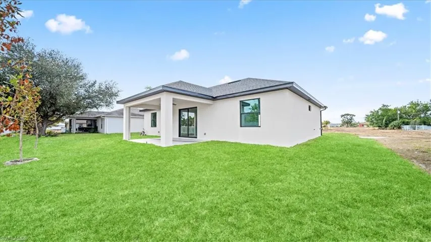 Rear view of property featuring a lawn, a patio area, and stucco siding