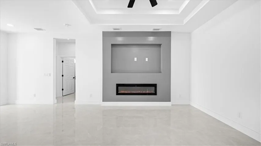 Unfurnished living room featuring a glass covered fireplace, a raised ceiling, and a ceiling fan