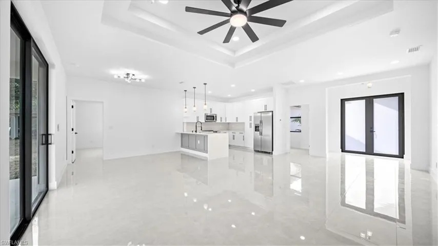 Unfurnished living room featuring plenty of natural light, french doors, recessed lighting, ceiling fan, and a tray ceiling