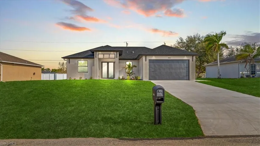 View of front of property featuring a yard, an attached garage, driveway, and stucco siding