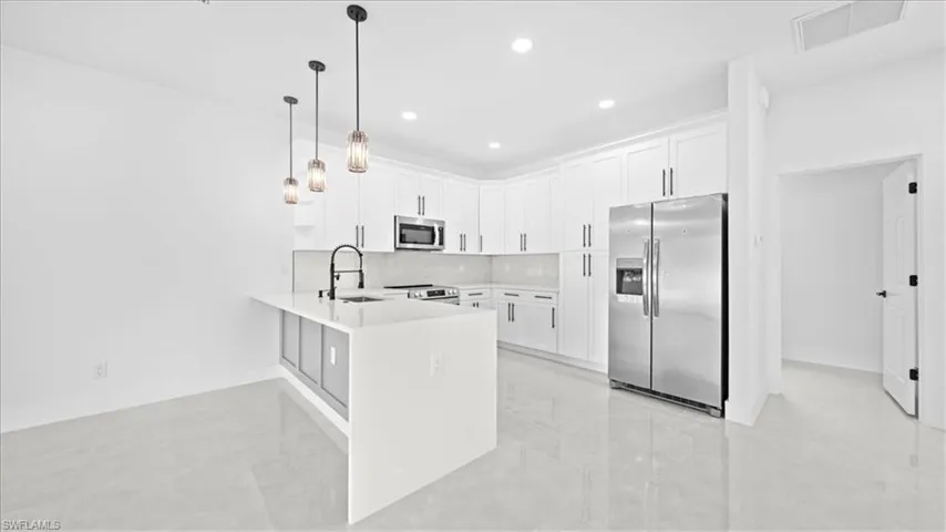 Kitchen with stainless steel appliances, a peninsula, white cabinets, decorative light fixtures, and a kitchen bar