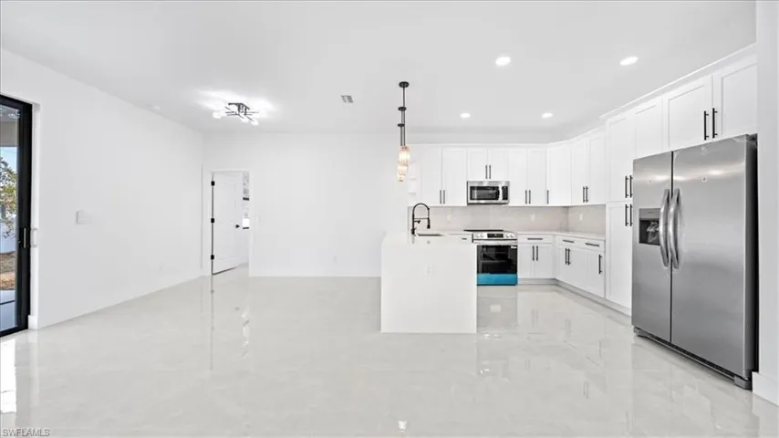 Kitchen with stainless steel appliances, white cabinetry, pendant lighting, an island with sink, and backsplash