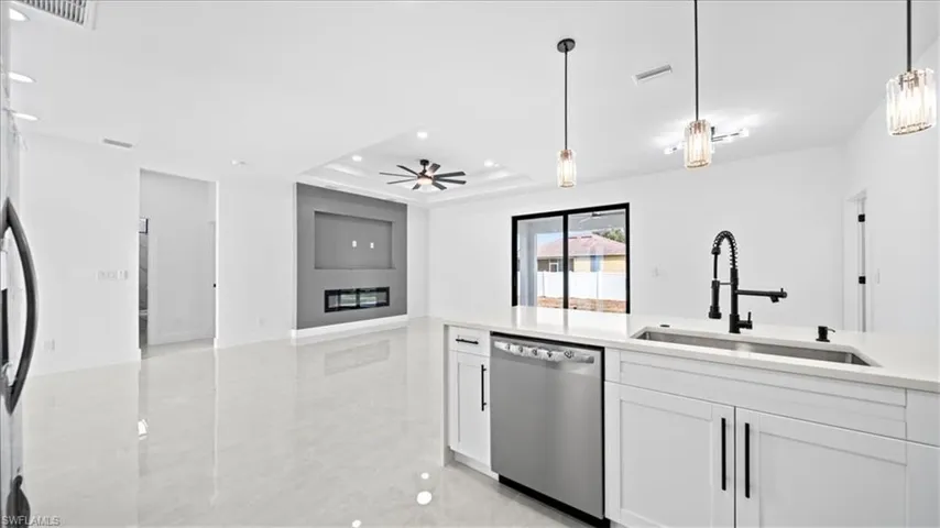 Kitchen with open floor plan, stainless steel appliances, pendant lighting, white cabinetry, and a tray ceiling