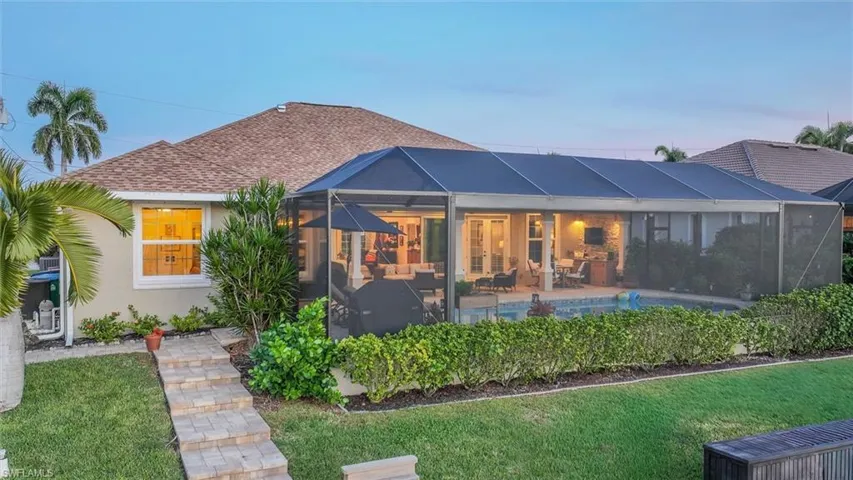 Back of property at dusk featuring an outdoor pool, a sunroom, glass enclosure, and stucco siding