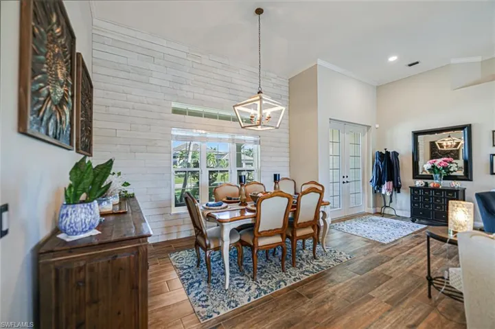 Dining room with french doors, wood finish floors, ornamental molding, a chandelier, and brick wall