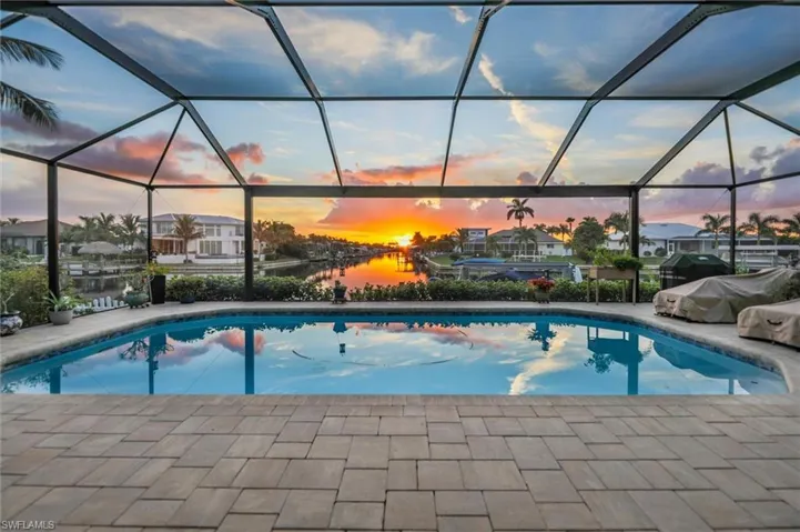 Pool at dusk with a sunroom, a water view, glass enclosure, and an outdoor pool