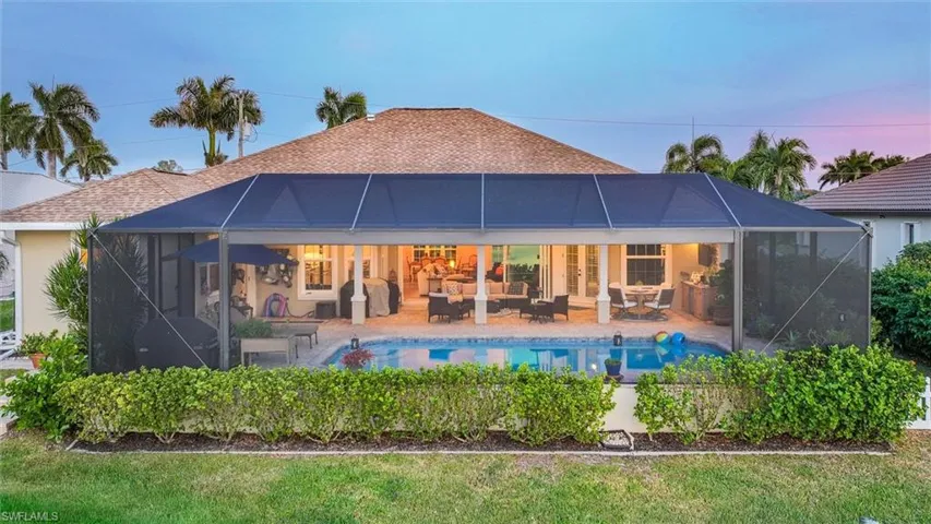 Rear view of property with a sunroom, glass enclosure, roof with shingles, and an outdoor pool