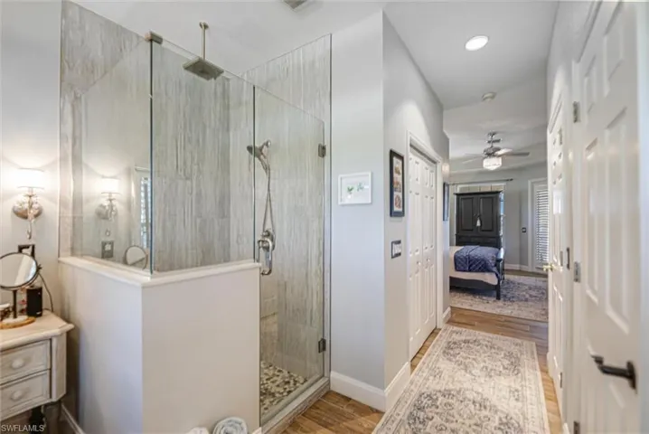 Full bathroom featuring connected bathroom, light wood-style floors, a shower stall, and a ceiling fan