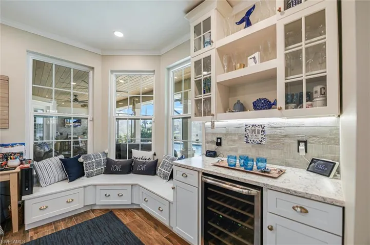 Bar area with beverage cooler, open shelves, white cabinetry, light stone counters, and ornamental molding