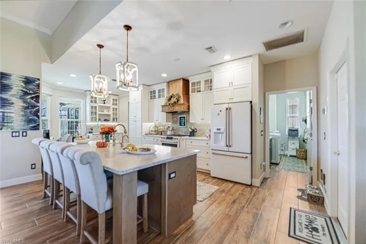 Kitchen with glass insert cabinets, high end appliances, white cabinets, a kitchen breakfast bar, and decorative light fixtures