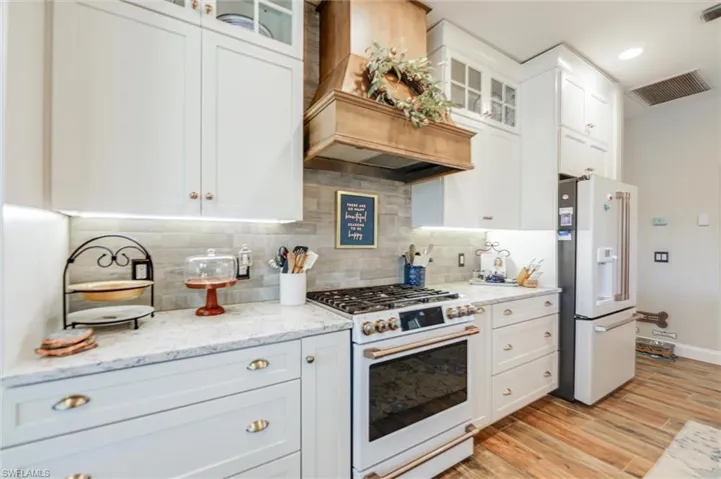 Kitchen with glass insert cabinets, high quality appliances, premium range hood, white cabinets, and recessed lighting