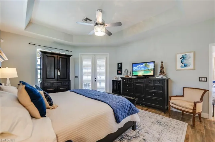 Bedroom featuring a tray ceiling, access to outside, dark wood finished floors, and a ceiling fan