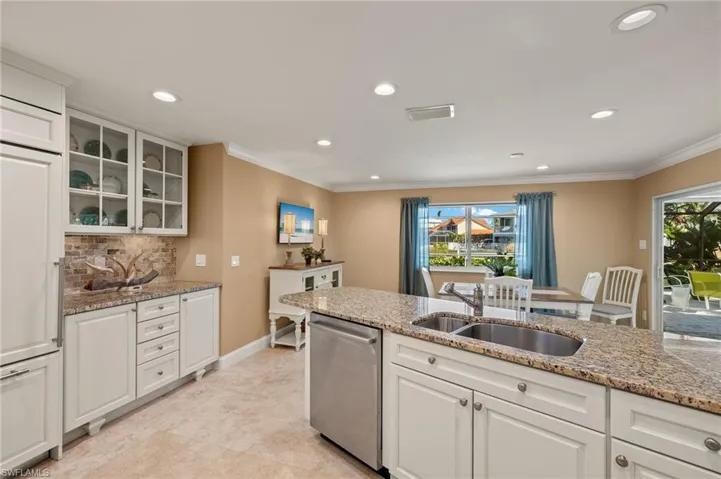 Kitchen with glass insert cabinets, white cabinets, light stone countertops, stainless steel dishwasher, and recessed lighting