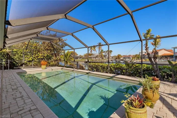 Outdoor pool with glass enclosure, a water view, a sunroom, and a patio