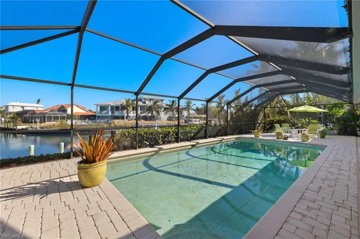 Outdoor pool featuring glass enclosure, a sunroom, a residential view, a water view, and a patio